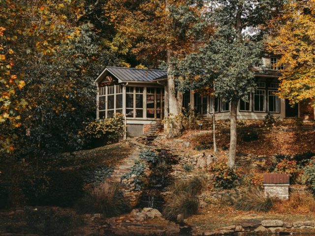 Beautiful fall scene of a cozy cottage surrounded by colorful autumn trees by a tranquil lake.