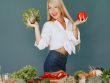 Cheerful woman in white shirt holding lettuce and pepper, celebrating fresh vegetables.